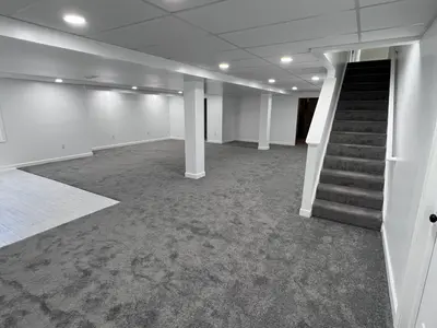 Finished basement with gray carpet, drop ceiling, staircase