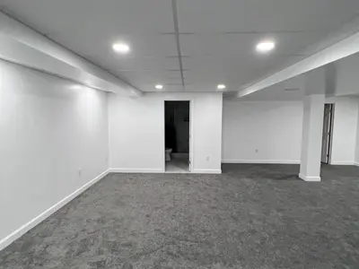 Empty finished basement room with bathroom doorway visible