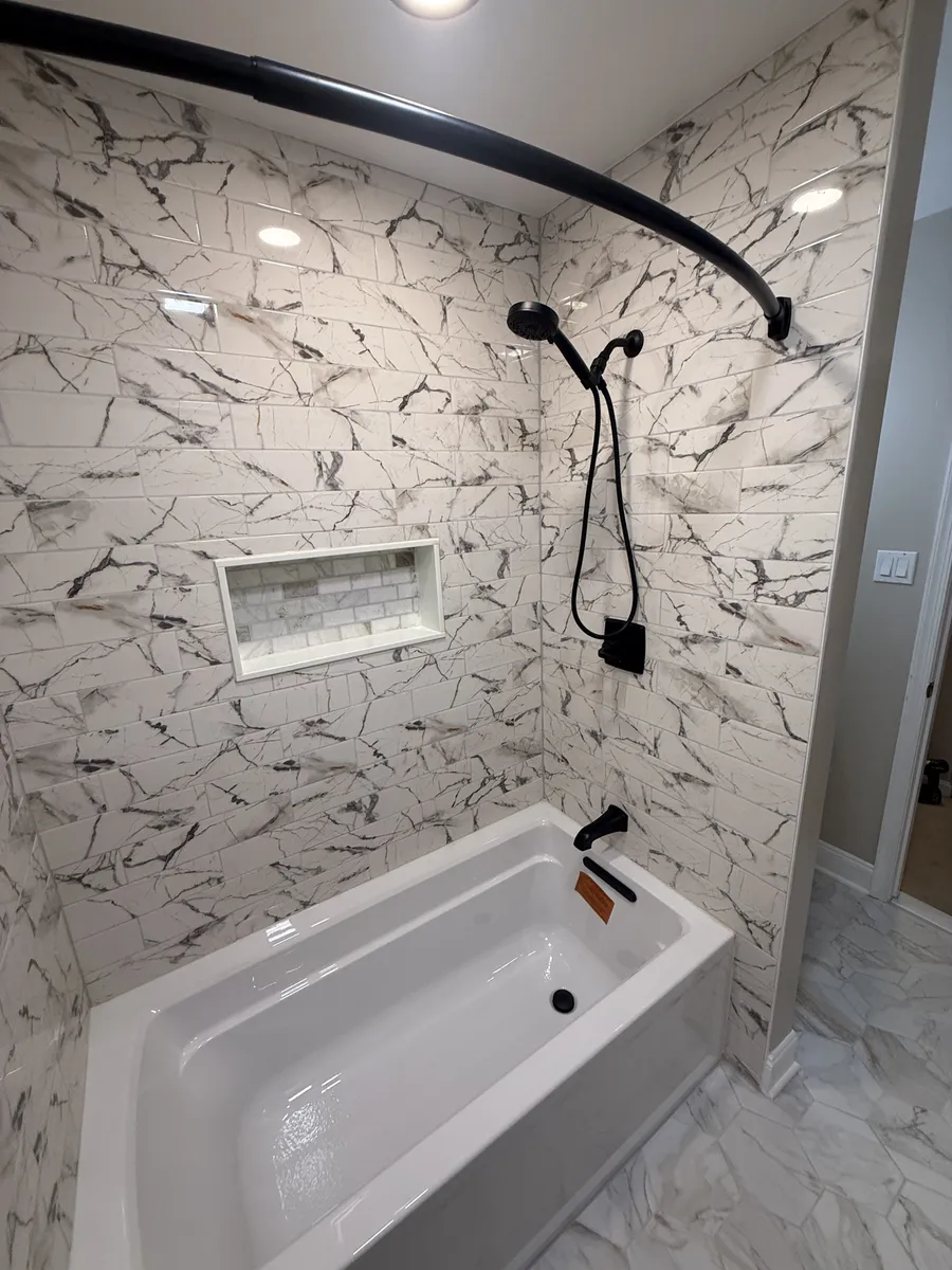 Marble-tiled shower tub with niche and black fixtures