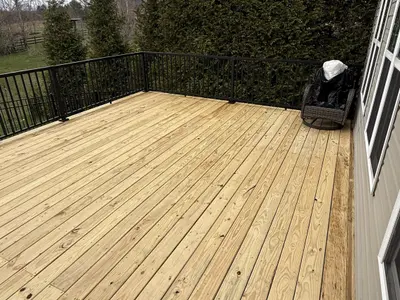 Empty wood plank deck with black railings overlooking yard