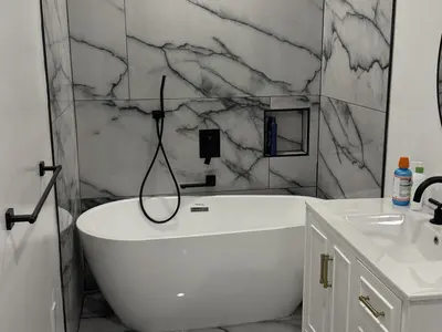 Freestanding white tub with marble walls and black fixtures