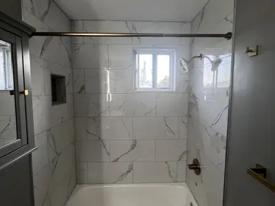 Tub shower with marble tile niche and gold rod