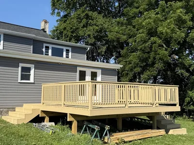 New wood deck construction with railings behind a gray-sided home