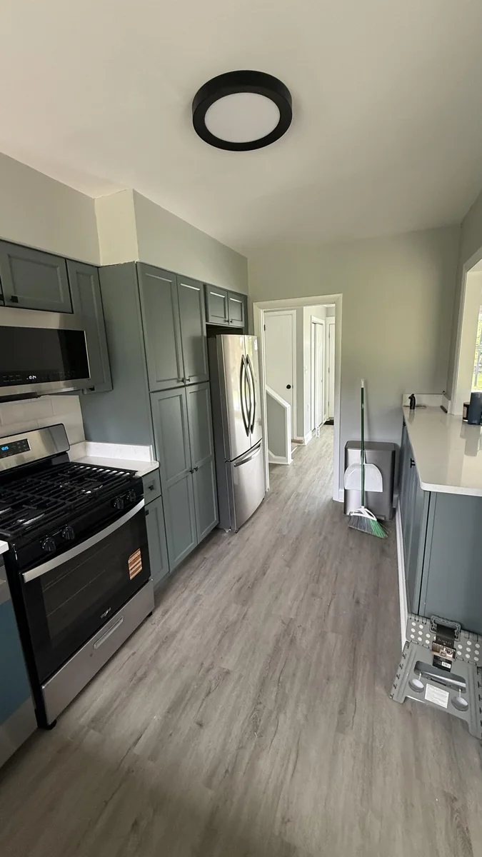 Remodeled galley kitchen with sage green cabinets and stainless gas range